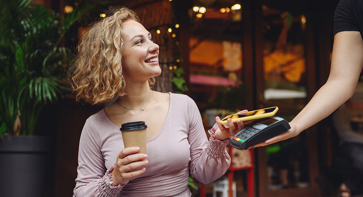 Young woman paying for coffee by tapping a phone on a terminal